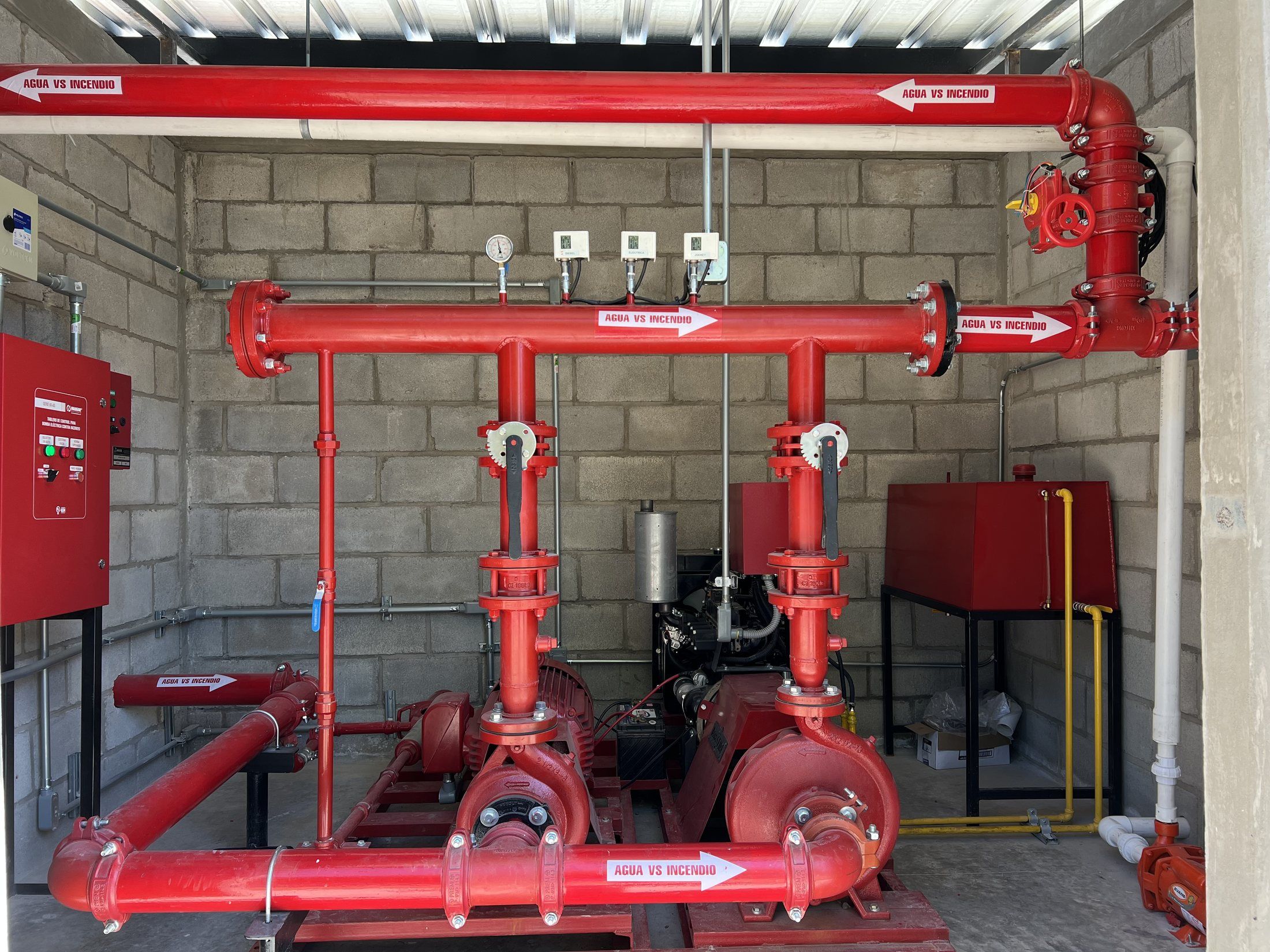 Cuarto de bombas contra incendio con equipo de bombeo, tablero de control y tubería roja rotulada «Agua vs incendio».