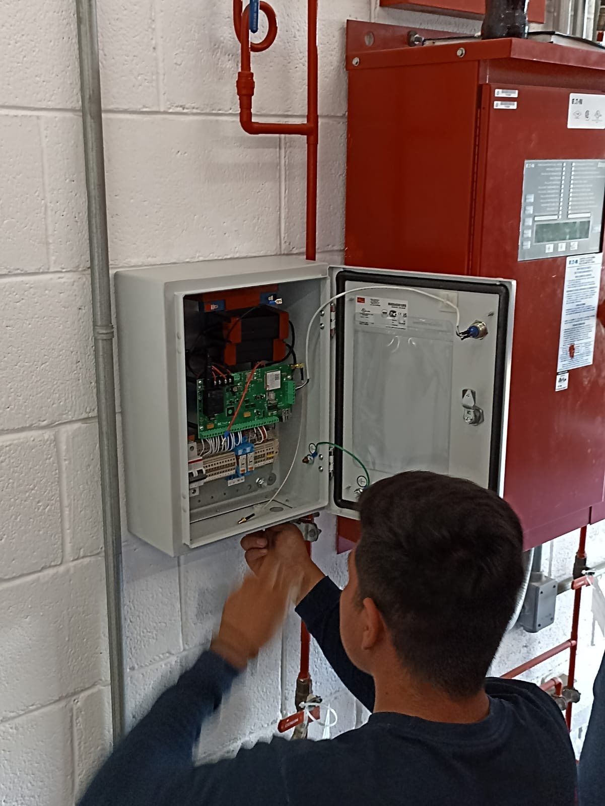 Técnico revisa el cableado dentro del gabinete de la unidad de monitoreo, junto al controlador de una bomba contra incendio.