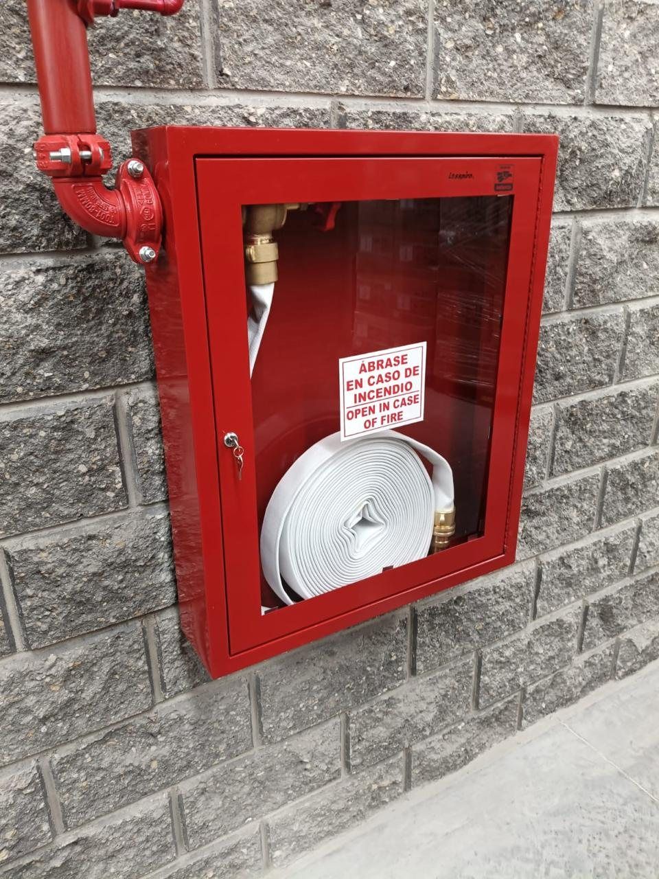 Gabinete de hidrante rojo con manguera y válvula, montado en muro de block.