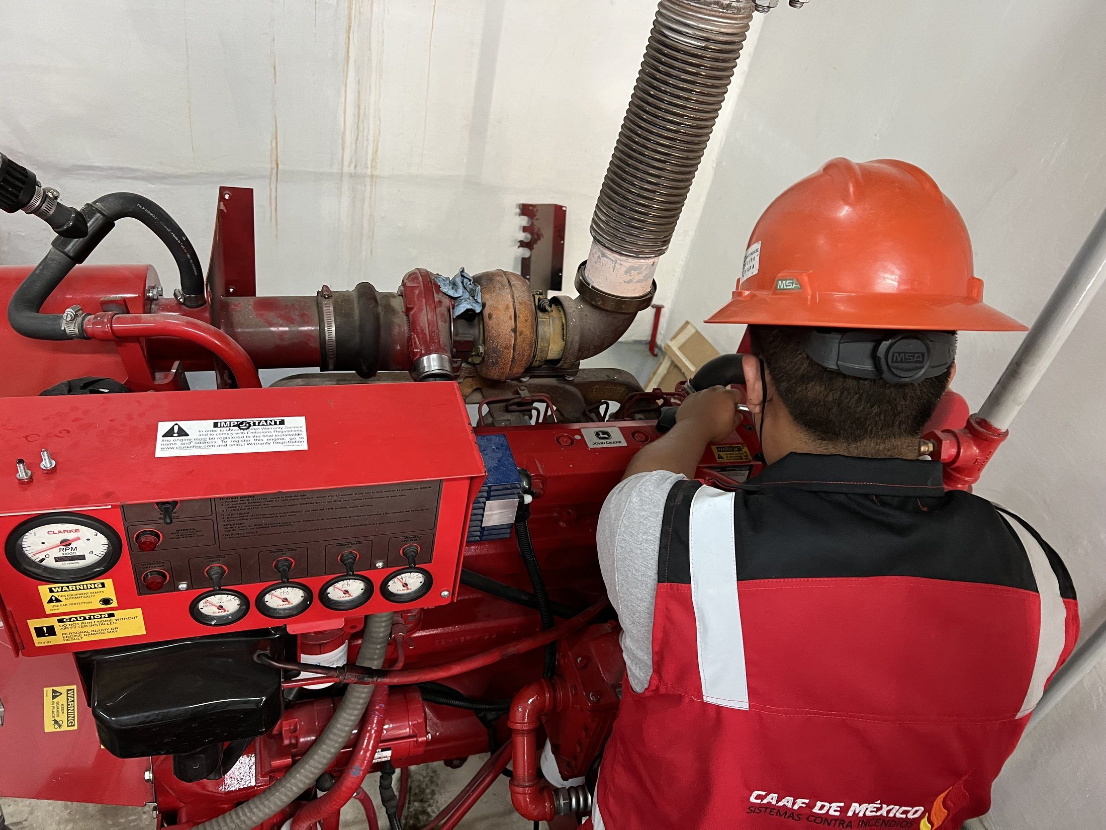Técnico de CAAF de México con casco naranja trabaja en el motor diésel Clarke de una bomba contra incendio; en primer plano, el tablero de instrumentos del motor.